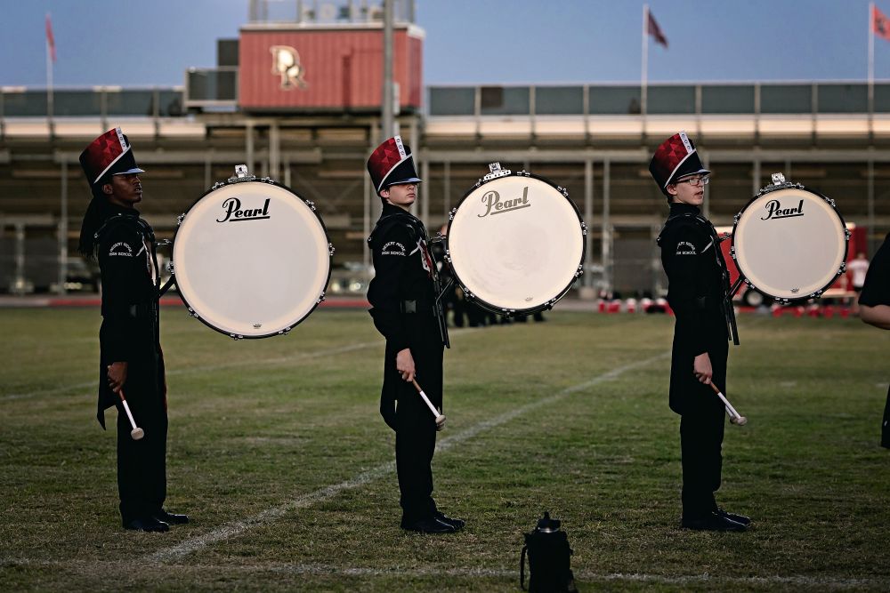 Three drummers standing at attention standing to the side, dressed in unifiorms